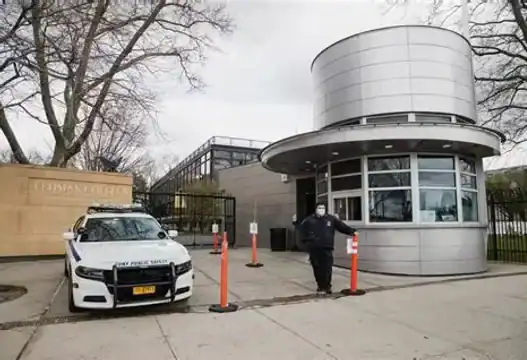 A security guard stands by a police car parked outside a modern building with bulletproof doors.