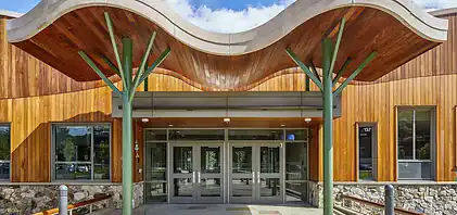 Modern building entrance with curved wood awning, ballistic glass doors, and green structural supports.
