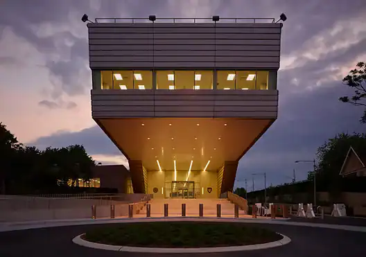 A modern building with bulletproof windows and bright lights stands at dusk, seen from the front entrance.