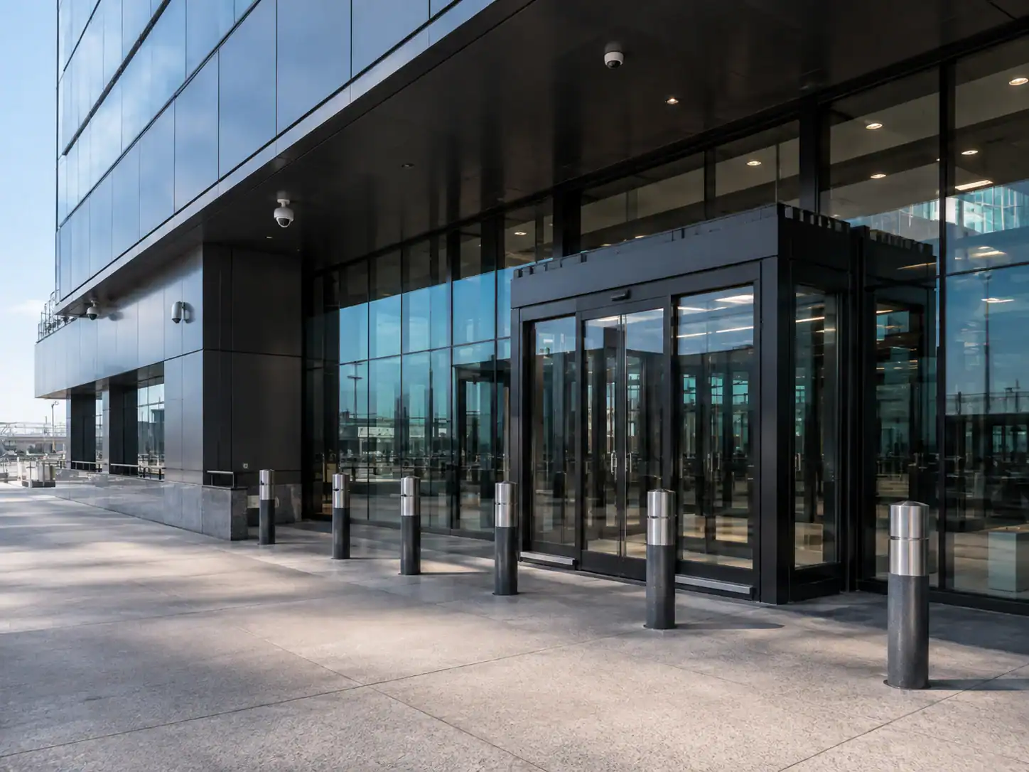 Modern glass office building entrance featuring automatic bullet resistant doors and several security bollards.